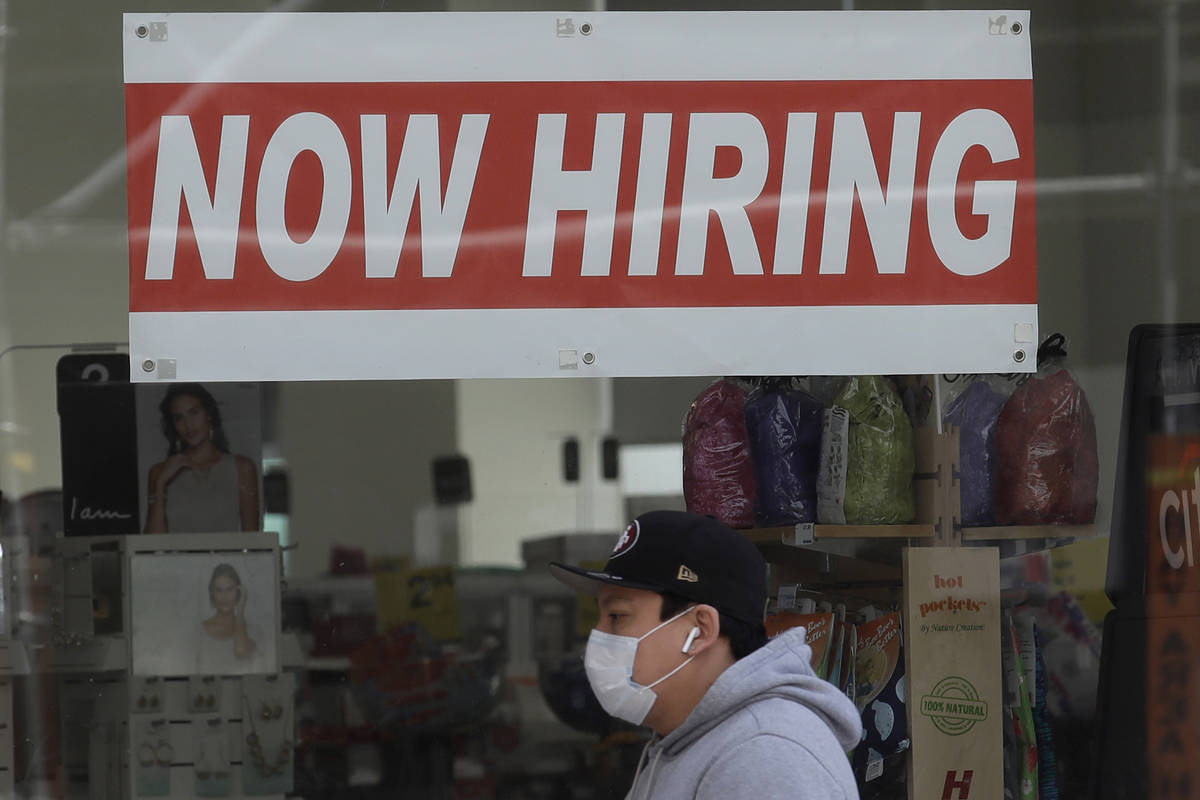 FILE - This May 7, 2020, file photo shows a man wearing a mask while walking under a Now Hiring ...