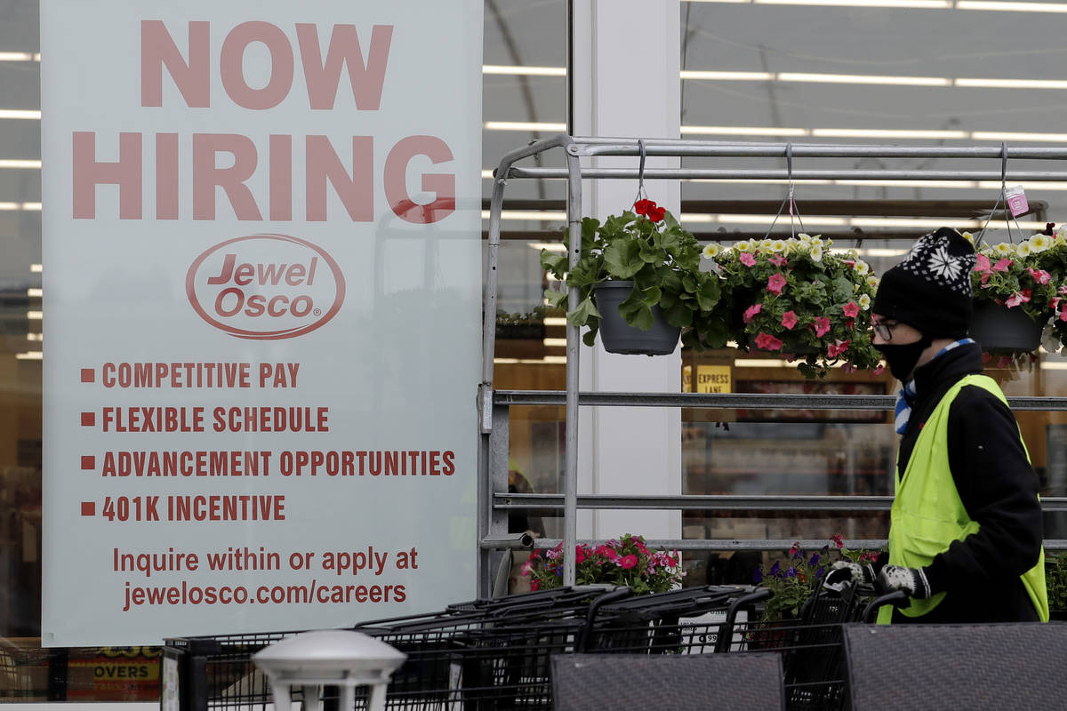 A man pushes carts as a hiring sign shows at a Jewel Osco grocery store in Deerfield, Ill., Thu ...