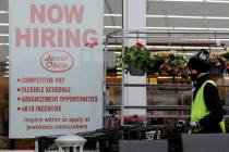 A man pushes carts as a hiring sign shows at a Jewel Osco grocery store in Deerfield, Ill., Thu ...