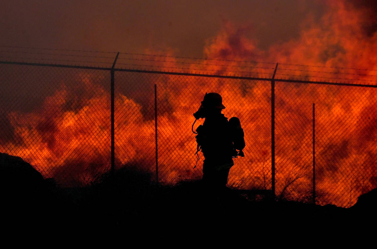 A firefighter walks past a wall of fire as multiple agencies battle a mulch and pallet fire bur ...