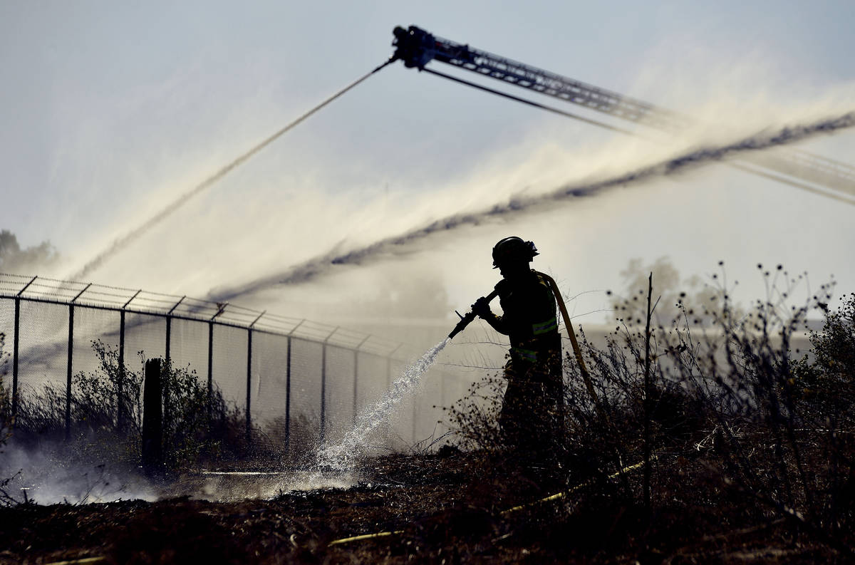 A firefighter sprays an area of a mulch and pallet fire burning out of control, fanned by Santa ...