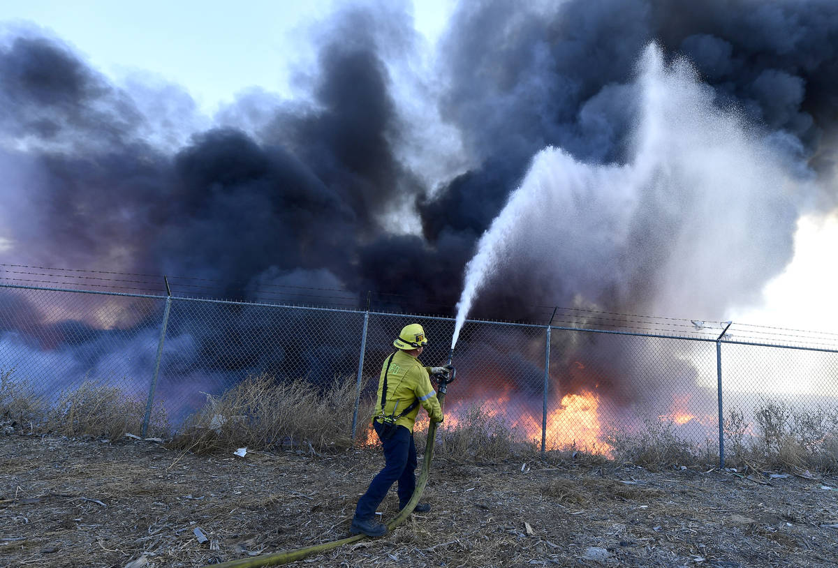A firefighter battles a mulch and pallet fire burning out of control, fanned by Santa Ana winds ...