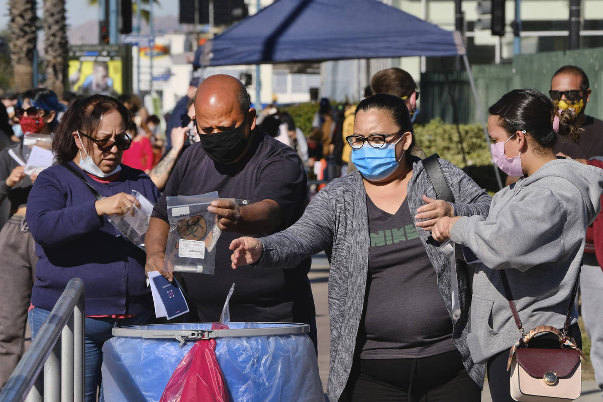 People drop their COVID-19 test kits into an intake receptacle after being tested at a site in ...