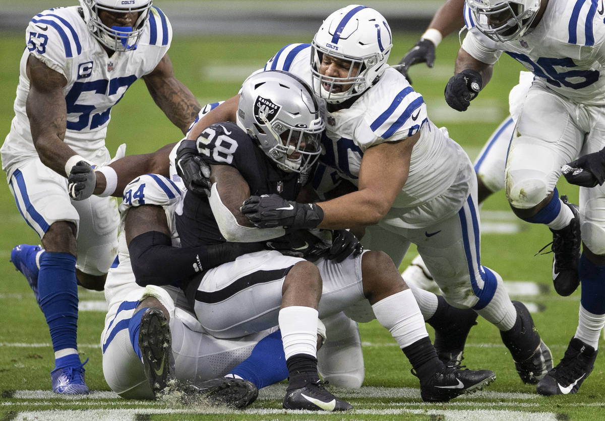 Raiders running back Josh Jacobs (28) is stacked up by Indianapolis Colts outside linebacker Da ...
