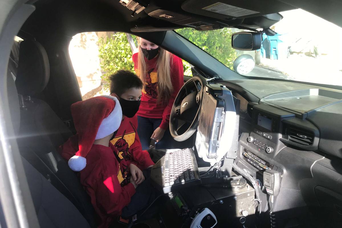 Nathan, 5, and Aiden, 8, sitting in a police car during the Santa Cops toy caravan drop off. (M ...