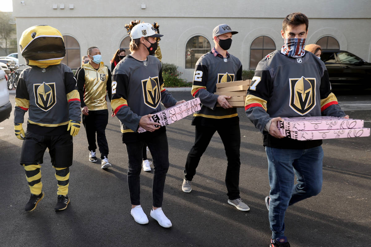 Golden Knights players Max Pacioretty, from right, Nick Holden and Zach Whitecloud load pizzas ...