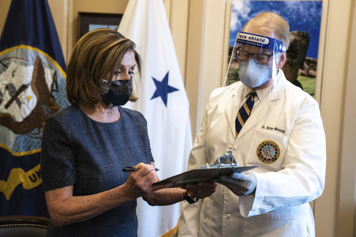 Speaker of the House Nancy Pelosi, D-Calif., signs a form next to Dr. Brian Monahan, attending ...