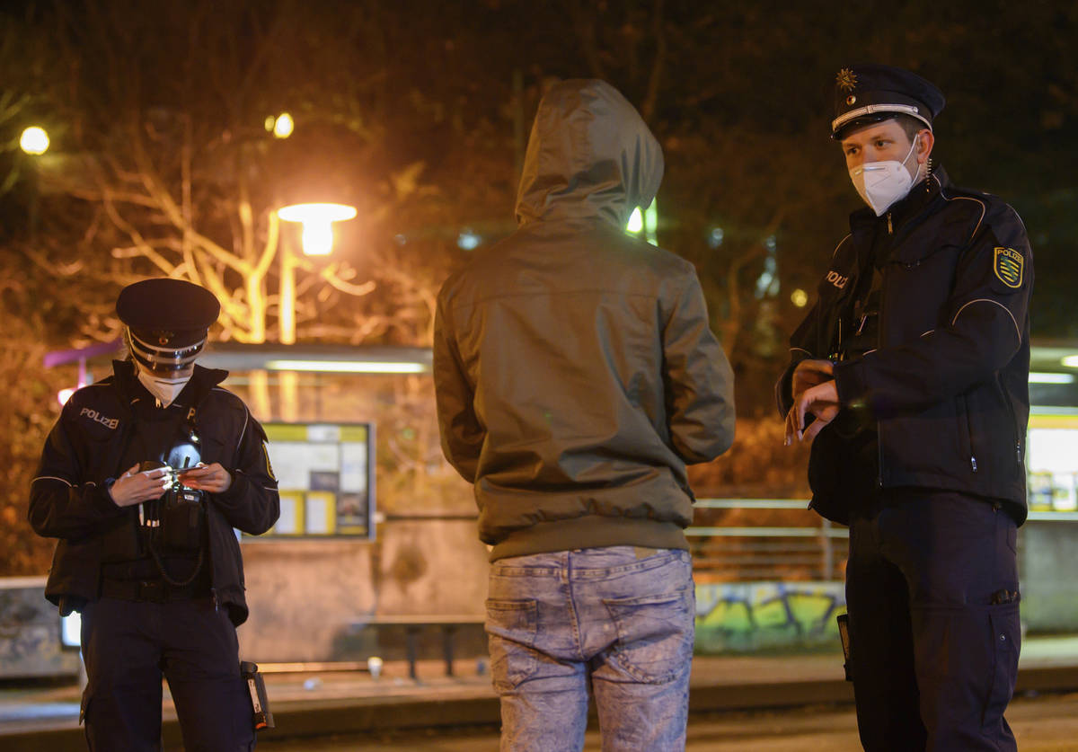 Police officers talk to a man during a curfew check at night in the Gorbitz district in Dresden ...