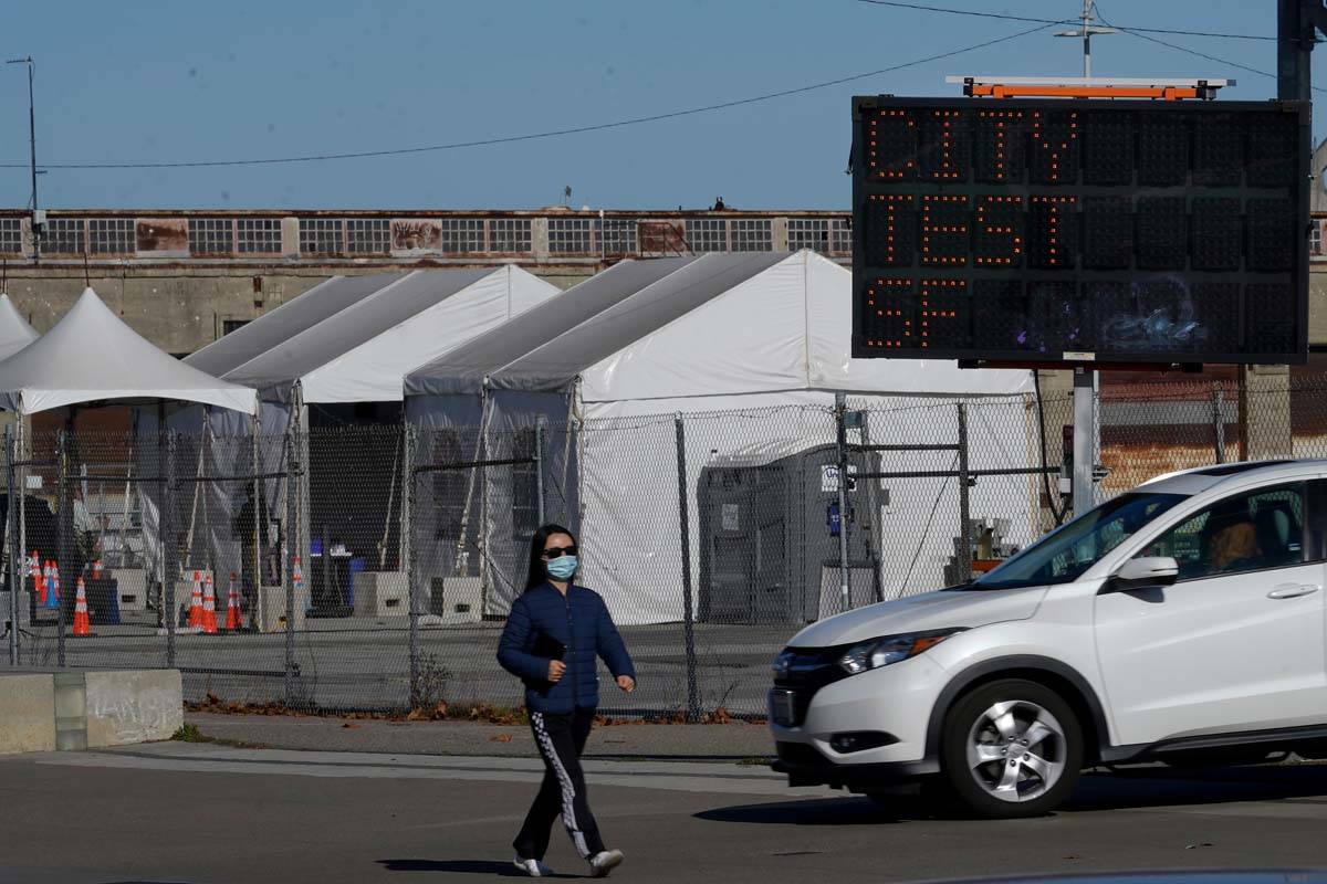 A pedestrian wears a face mask while walking past a car exiting the CityTestSF at Pier 30/32 CO ...