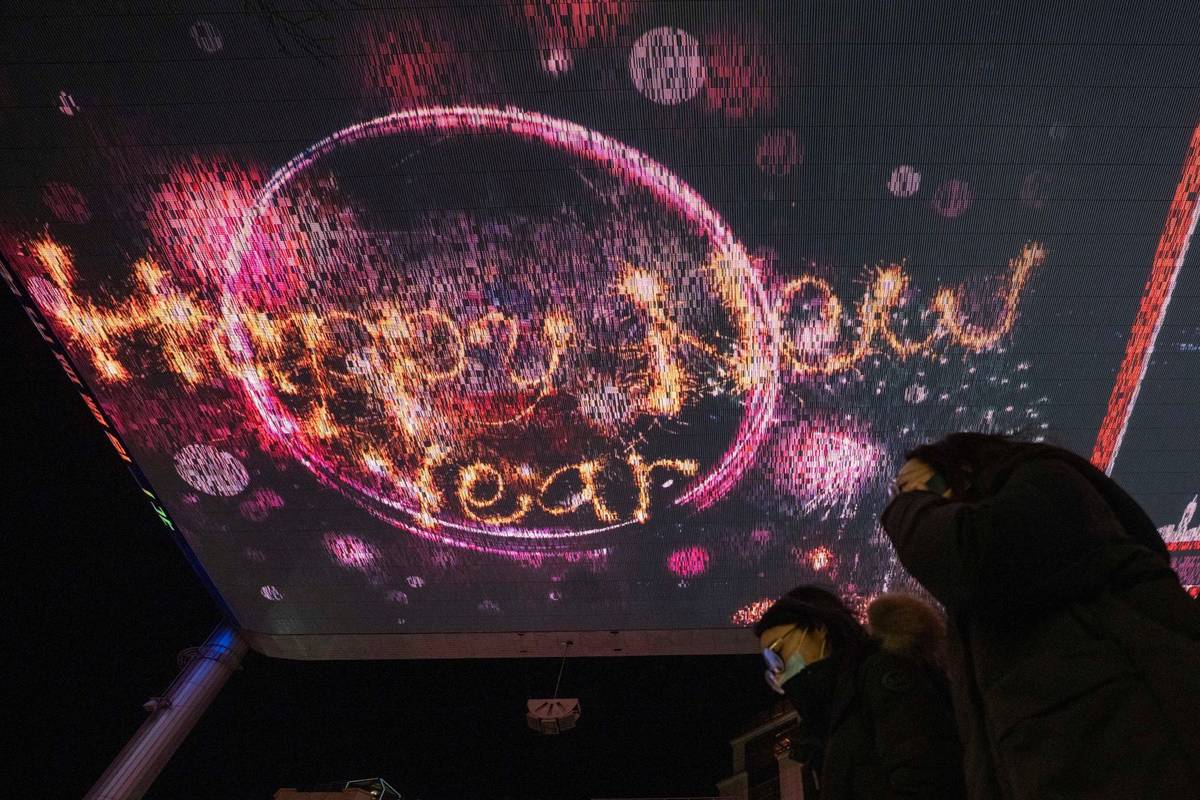 Visitors to a mall passes by Happy New Year greetings shown on a giant screen in Beijing Thursd ...