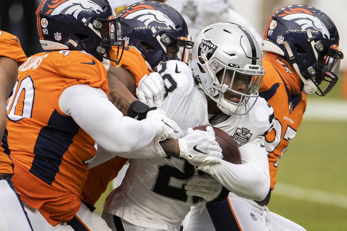 Raiders running back Josh Jacobs (28) drives forward with a group of Denver Broncos on his back ...