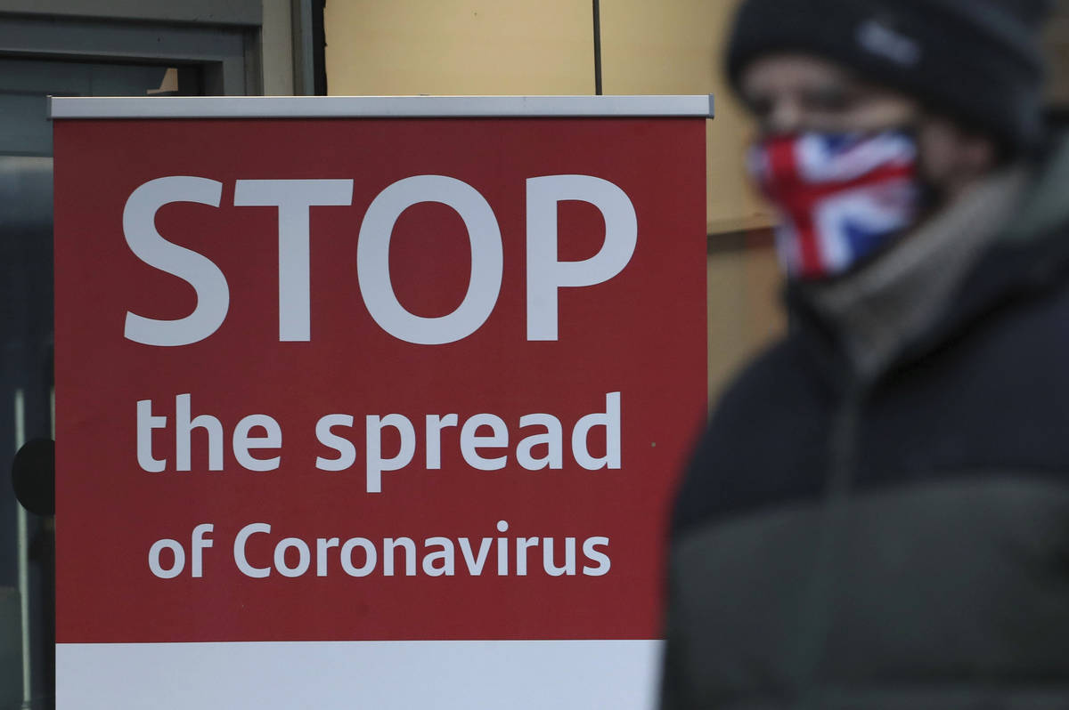 A man wearing a British union flag face mask walks past a coronavirus advice sign outside a ban ...