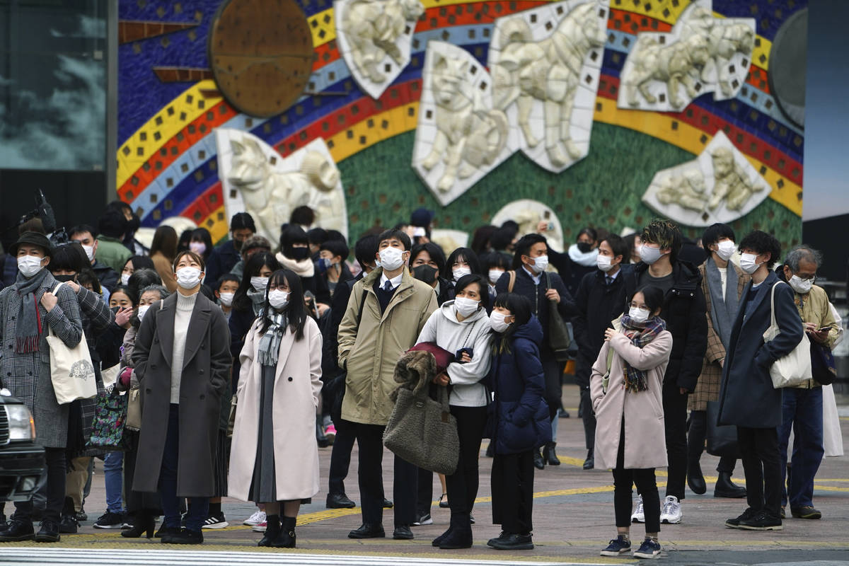 People wearing protective masks to help curb the spread of the coronavirus wait for traffic lig ...
