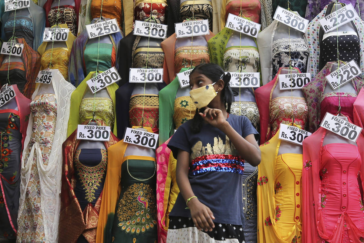 A girl wearing a face mask as a precaution against the coronavirus walks past a display of garm ...