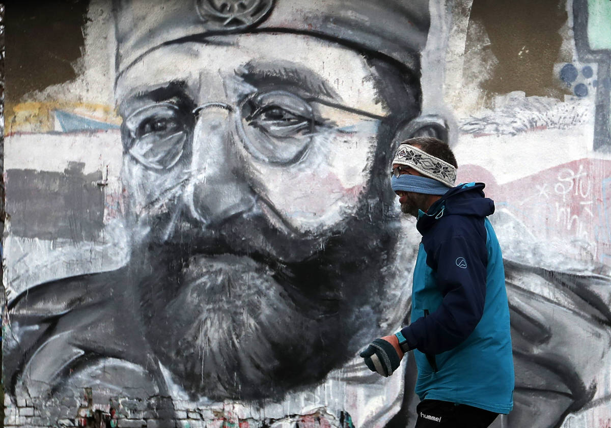A man wearing a face mask to protect against coronavirus runs past a wall painted with portrait ...