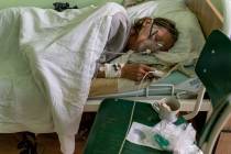 A patient with coronavirus breathes wearing an oxygen mask in an intensive care unit at the hos ...