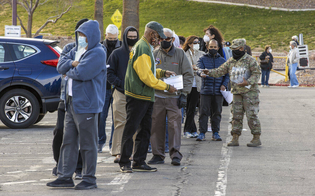 People receive paperwork while waiting in a long line in the parking lot at the Cashman Center ...