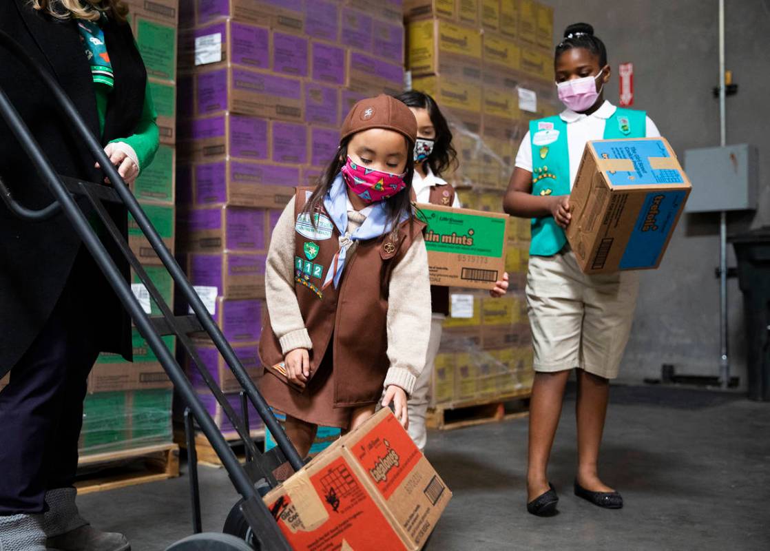 Girl scouts Penelope W., 7, moves a box of Girl Scout Cookies onto a dolly held by Kimberly Tru ...