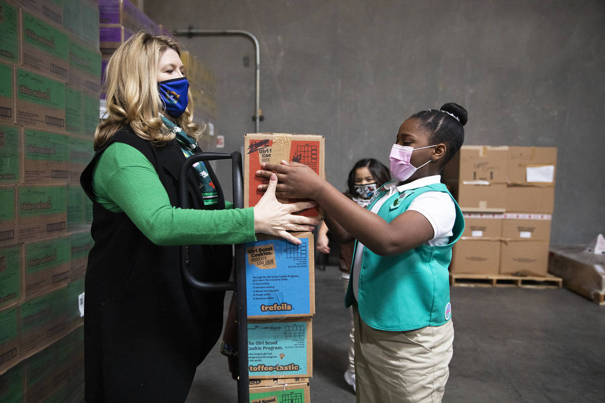 Girl Scout Aliyah H., 9, moves a box of Girl Scout Cookies onto a dolly held by Kimberly Trueba ...