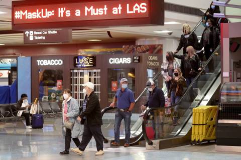 Masked travelers walk through Terminal 1 at McCarran International Airport in Las Vegas Friday, ...