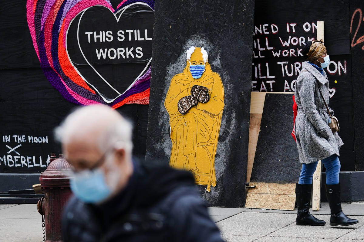 People wearing face masks as a precaution against the coronavirus walk past a depiction of Sen. ...