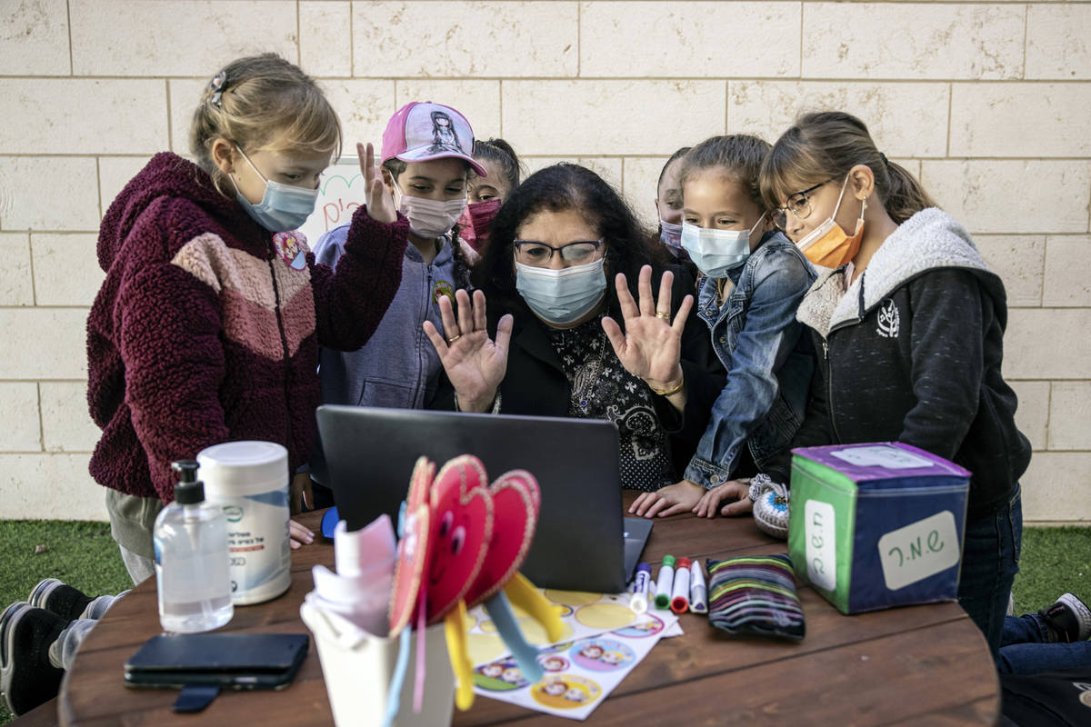 A teacher and her students wave to their classmates on a computer doing remote learning, from t ...