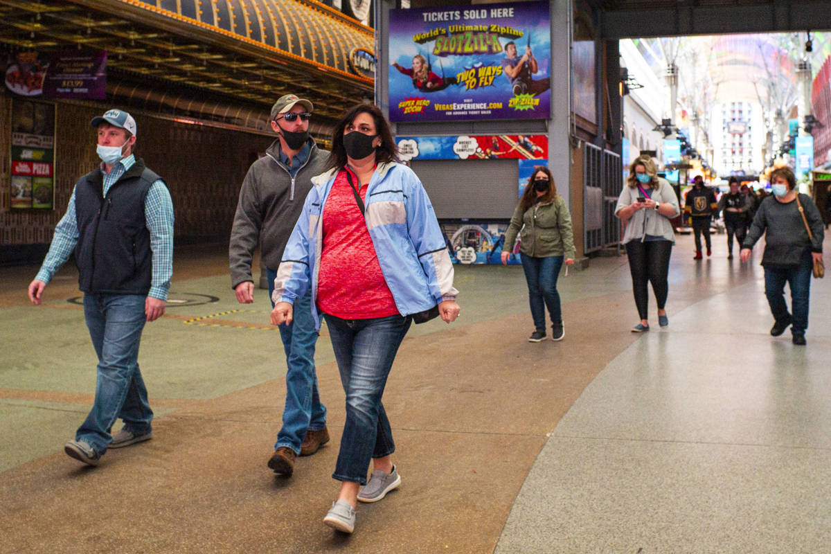 People wearing face masks, including two worn improperly below the nose, are seen walking along ...