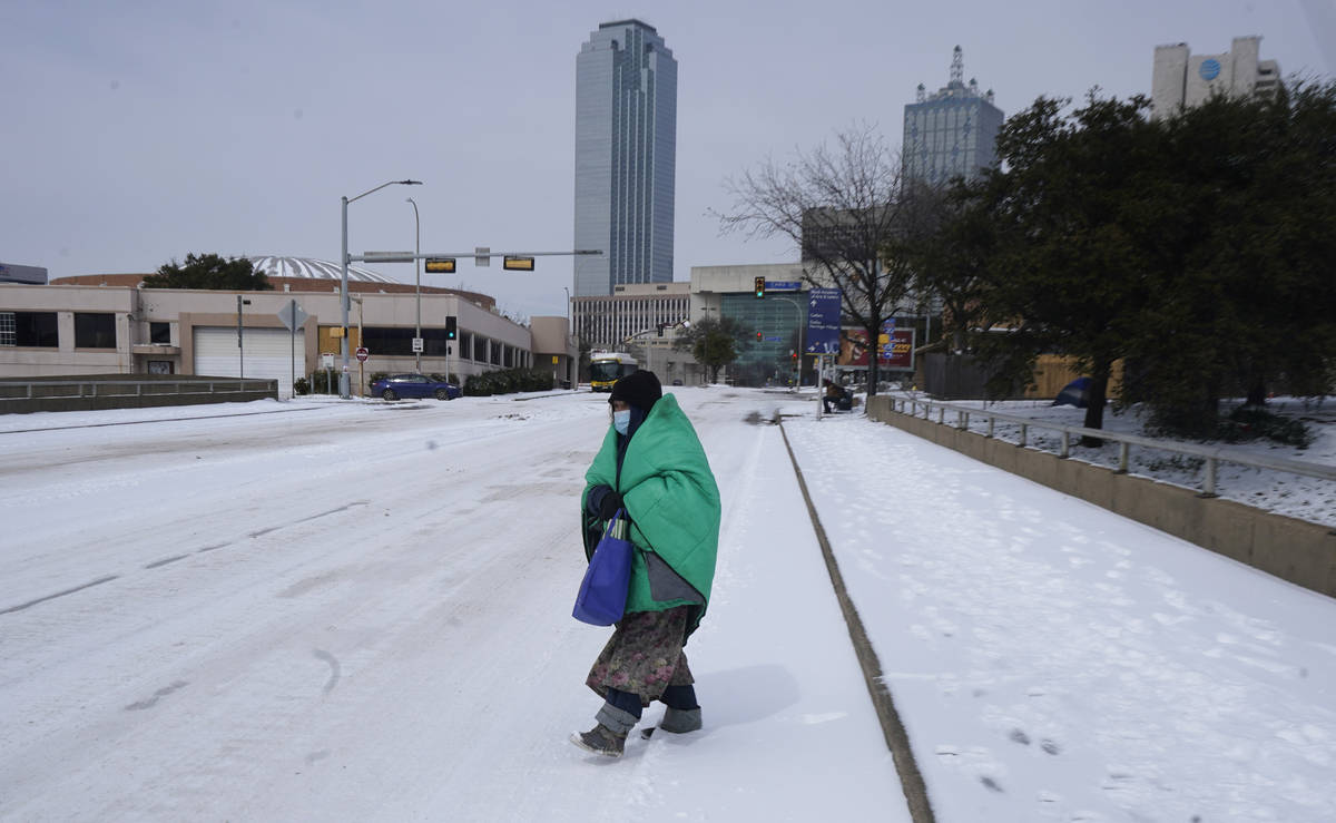 A woman wrapped in a blanket crosses the street near downtown Dallas, Tuesday, Feb. 16, 2021. ...