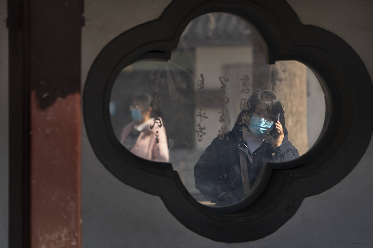 A woman wearing a face mask to protect against the spread of the coronavirus uses her smartphon ...