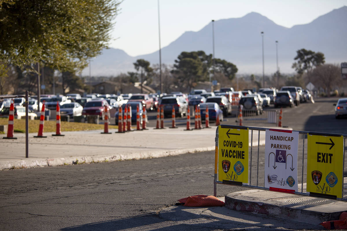 Signs indicate where to go to get a COVID-19 vaccine with a full parking lot in the background ...