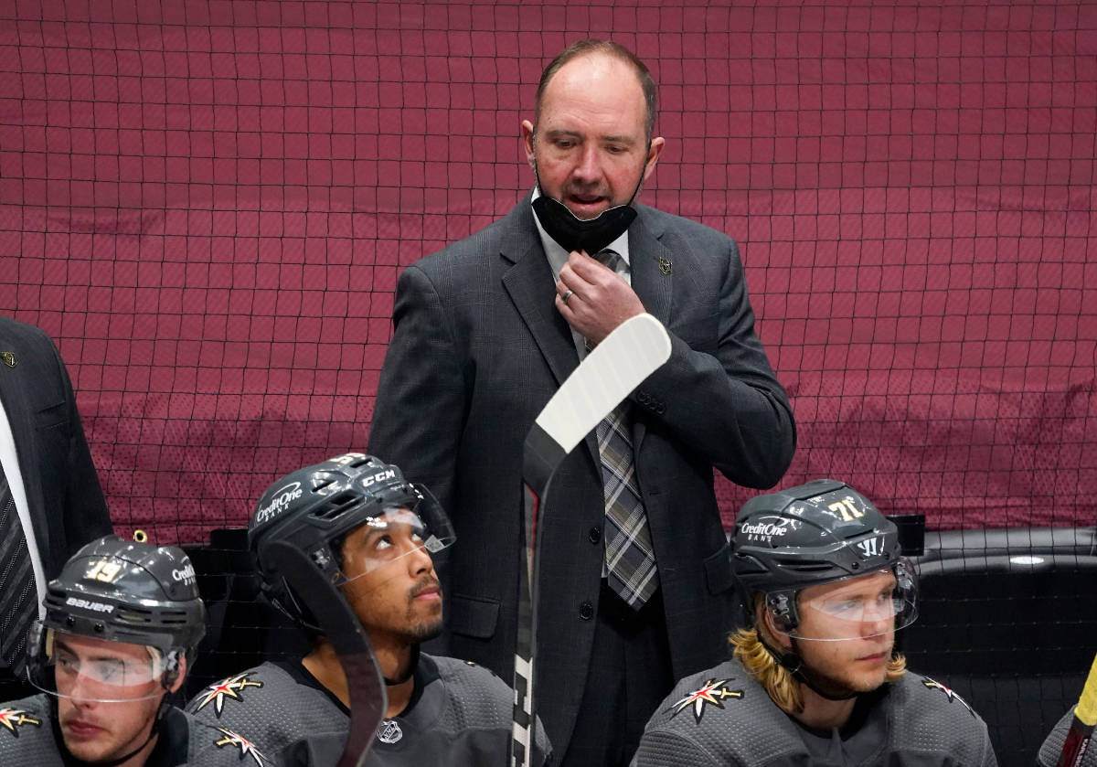 Vegas Golden Knights head coach Peter DeBoer, back, pulls down his mask to talk to his players ...