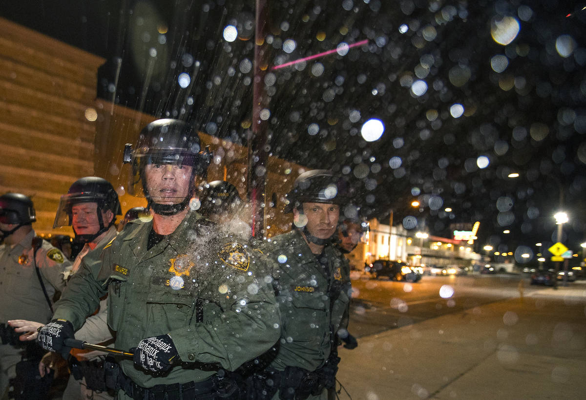 A Las Vegas police officer is struck on the shoulder by a water bottle during clashes with prot ...