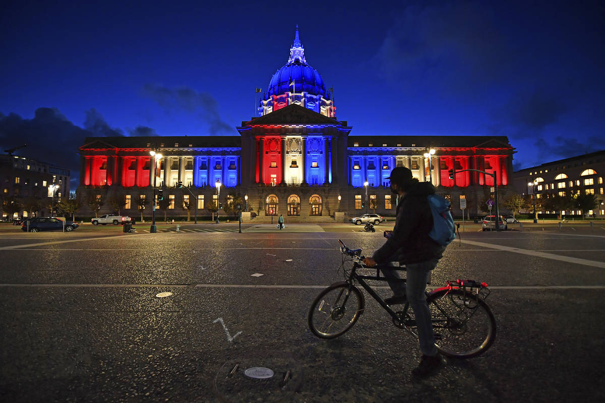 A bicyclist stops to admire the red, white and blue lights illuminating San Francisco City Hall ...
