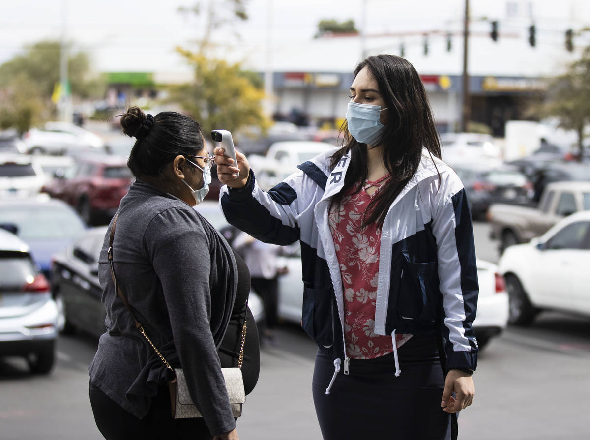 A woman gets her temperature taken by Ezabai Coronado, a volunteer, before taking her COVID-19 ...