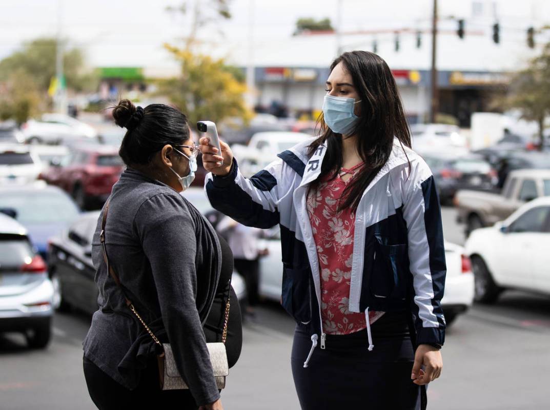A woman gets her temperature taken by Ezabai Coronado, a volunteer, before taking her COVID-19 ...