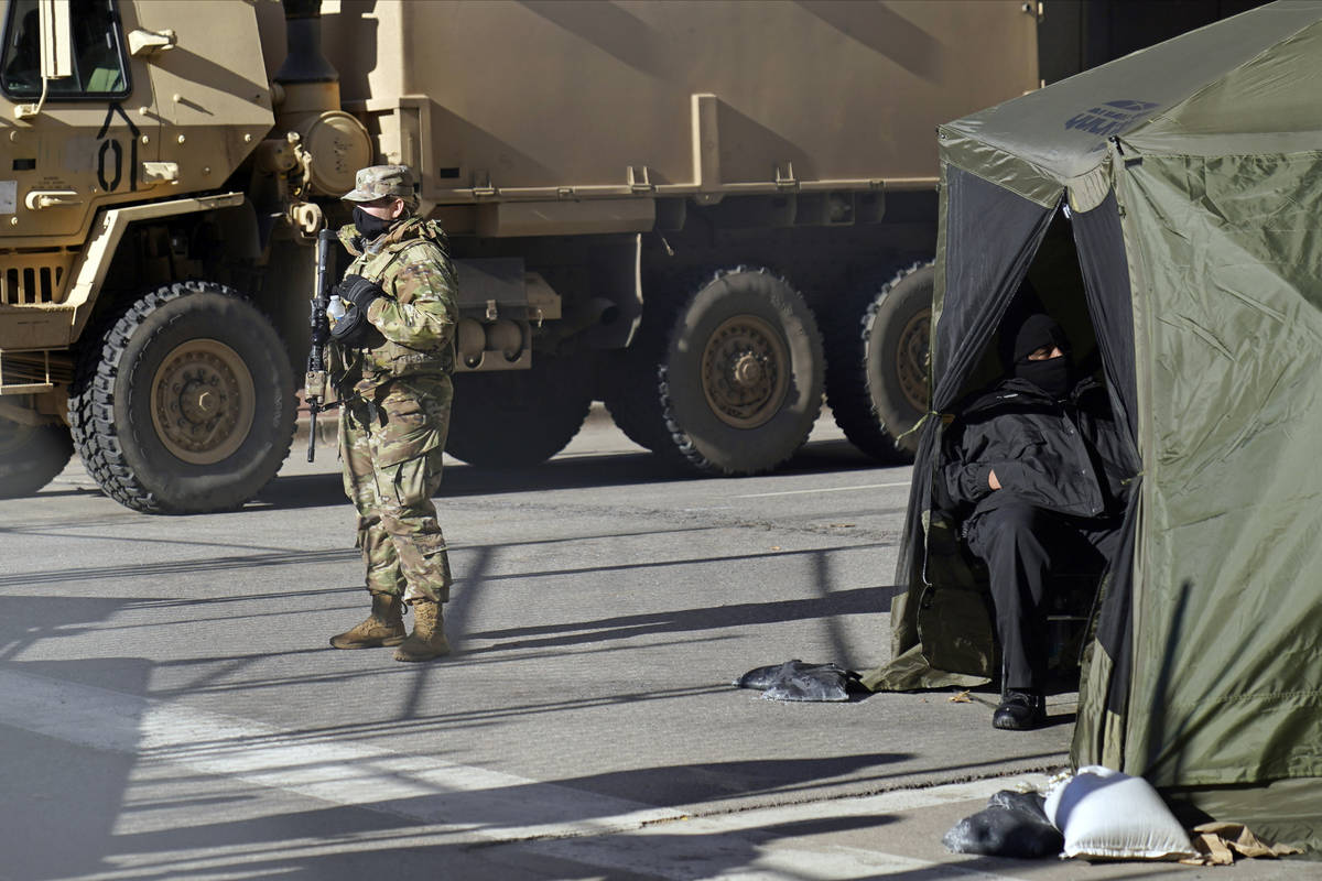 A National Guard soldier, left, stands guard while another security person, right, relaxes in a ...