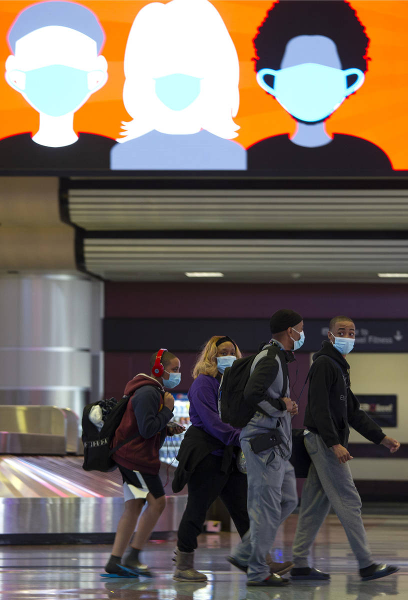 People move throughout baggage claim, wearing personal protective equipment to prevent the spre ...