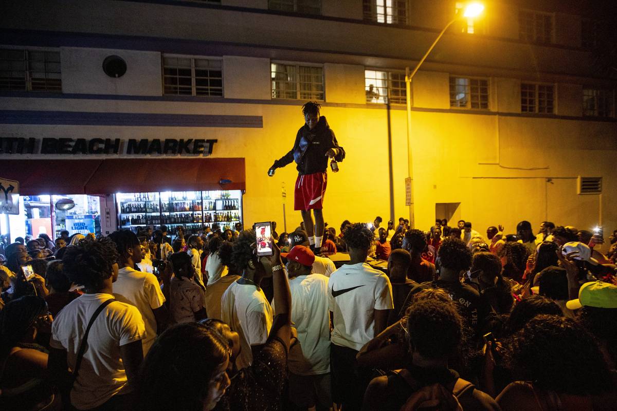 A man stands on a car as crowds defiantly gather in the street while a speaker blasts music an ...