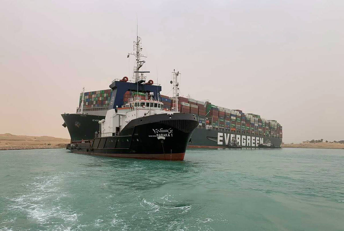 In this photo released by the Suez Canal Authority, a boat navigates in front of a massive carg ...