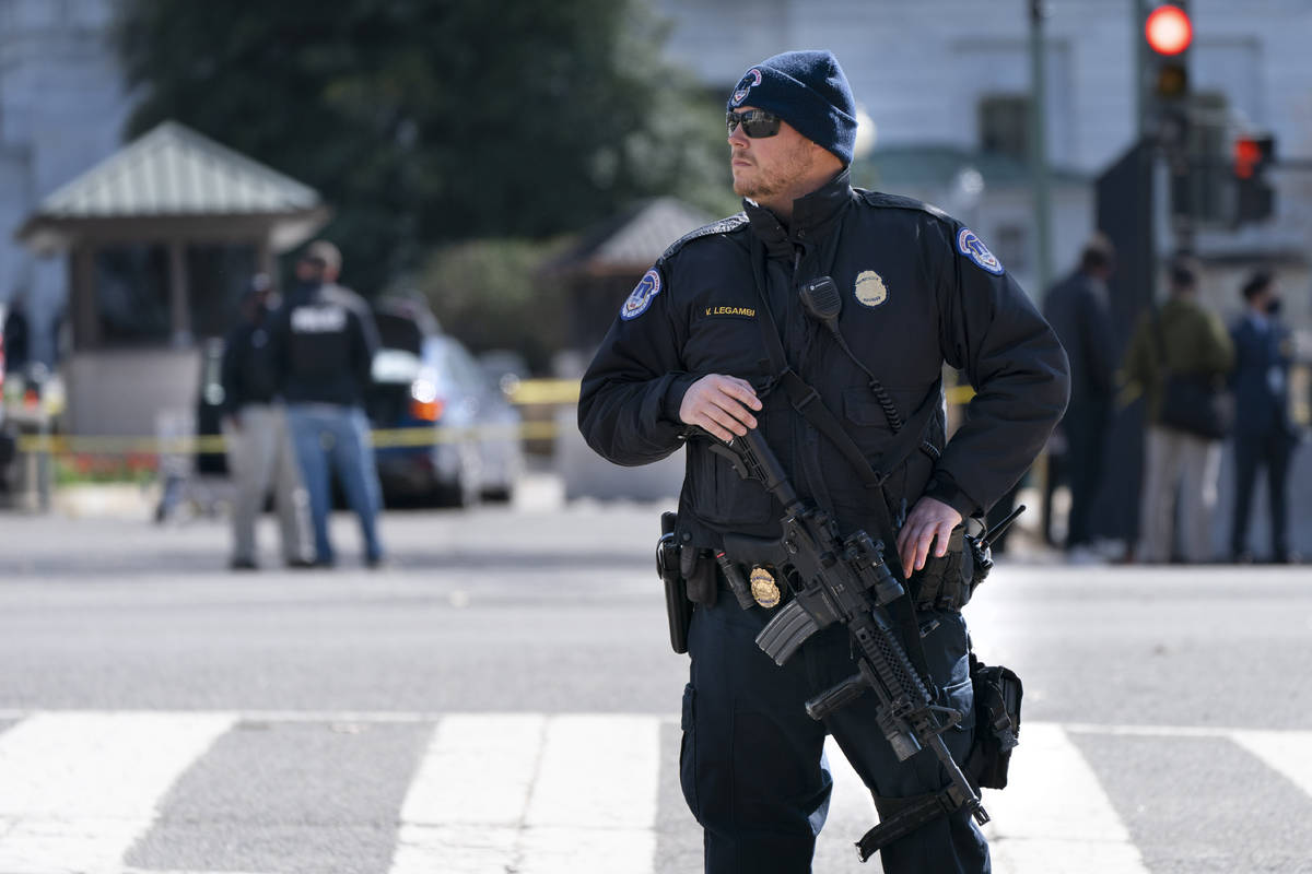 A Capitol Police officer patrols with a rifle at the site where a car crashed into a barrier on ...