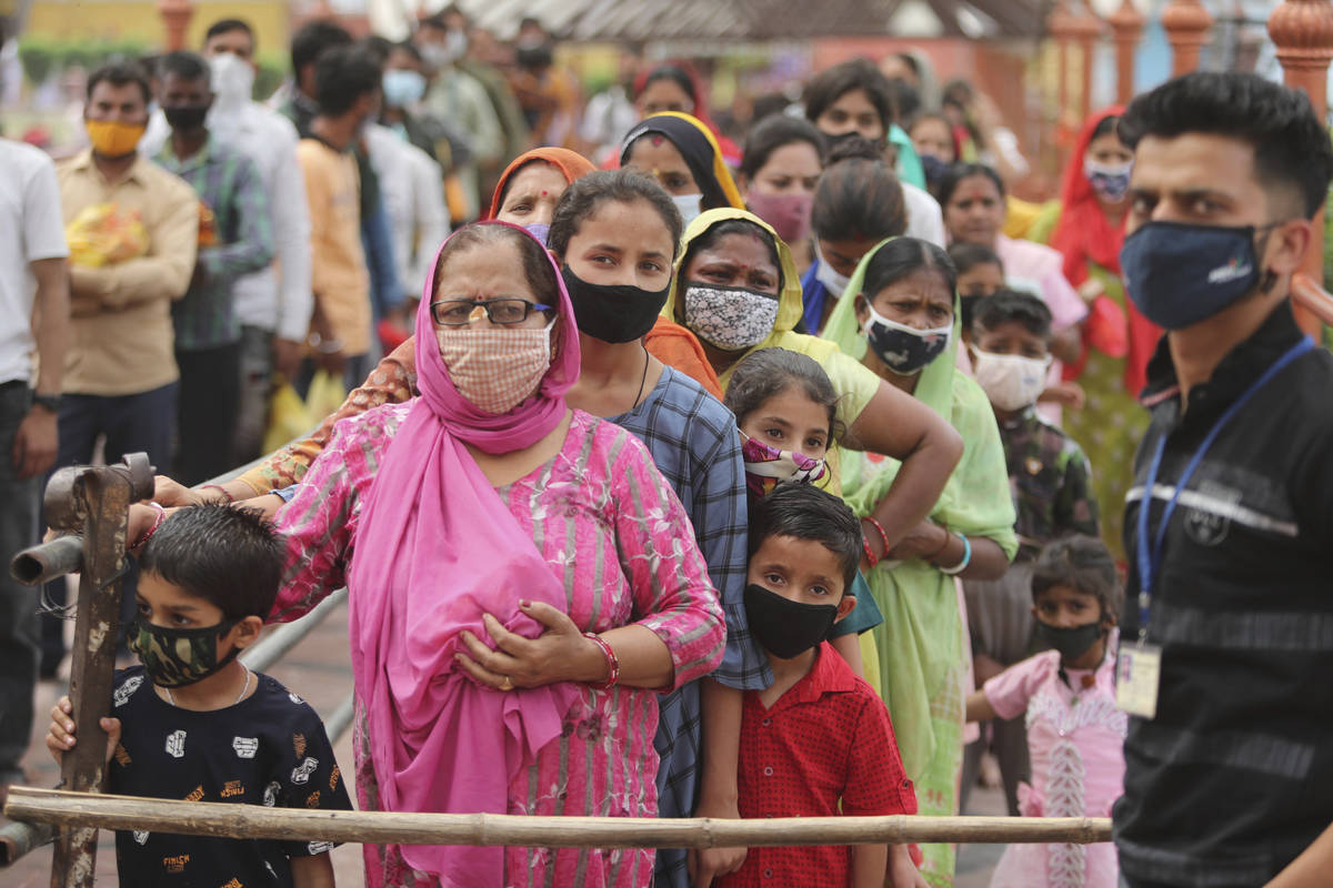 Hindu devotees wearing face masks as a precautionary measure against the coronavirus stand in a ...