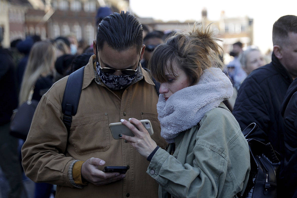 People watch live coverage on a phone outside Windsor Castle during the funeral of Britain's Pr ...