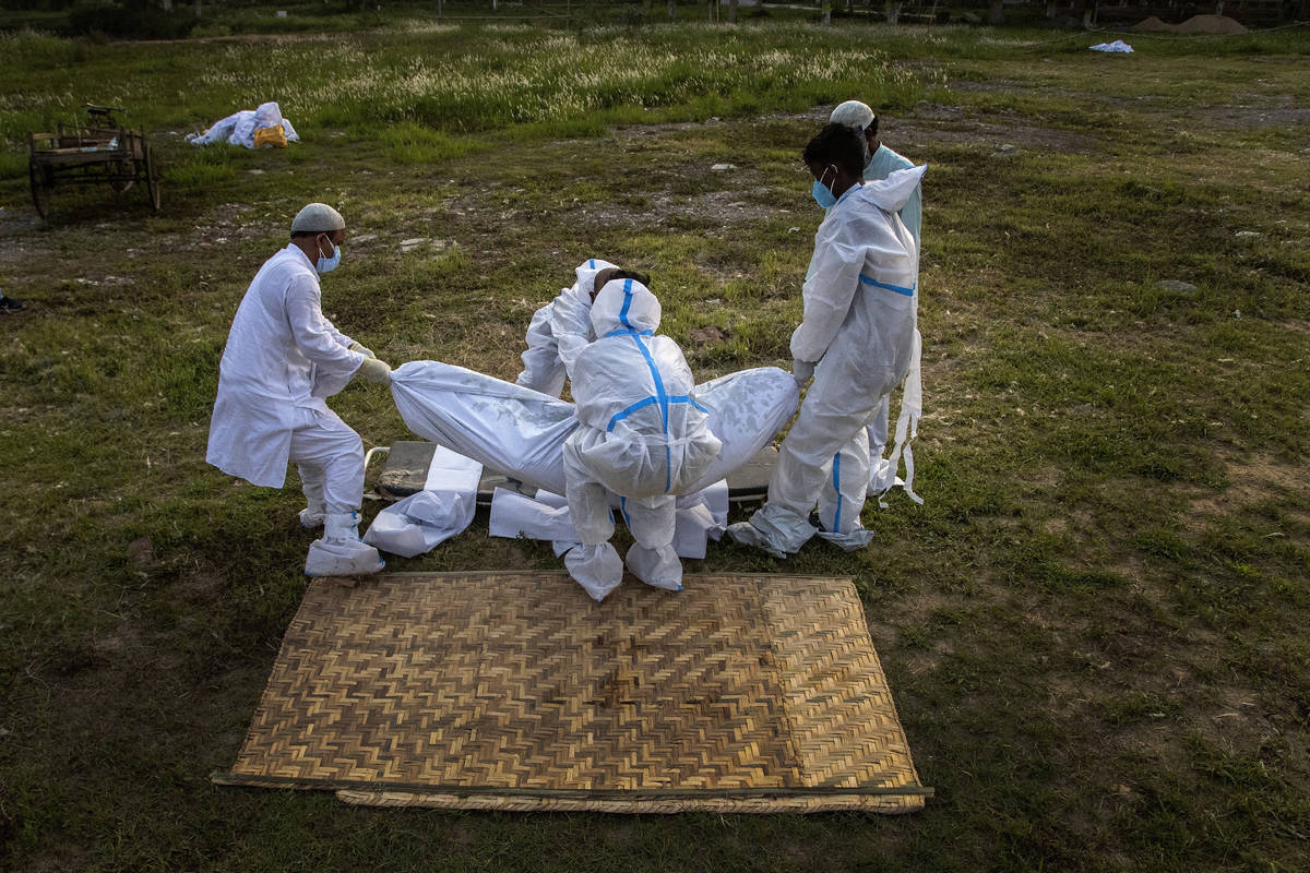 Relatives and municipal workers prepare to bury the body of a person who died of COVID-19 in Ga ...