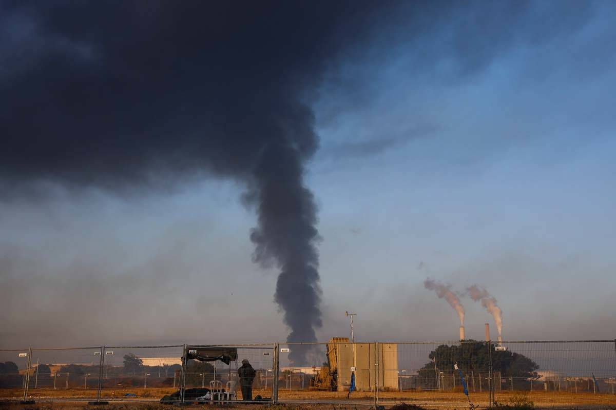 An Israeli soldier stands guard next to an Iron Dome air defense system as smoke rises from an ...