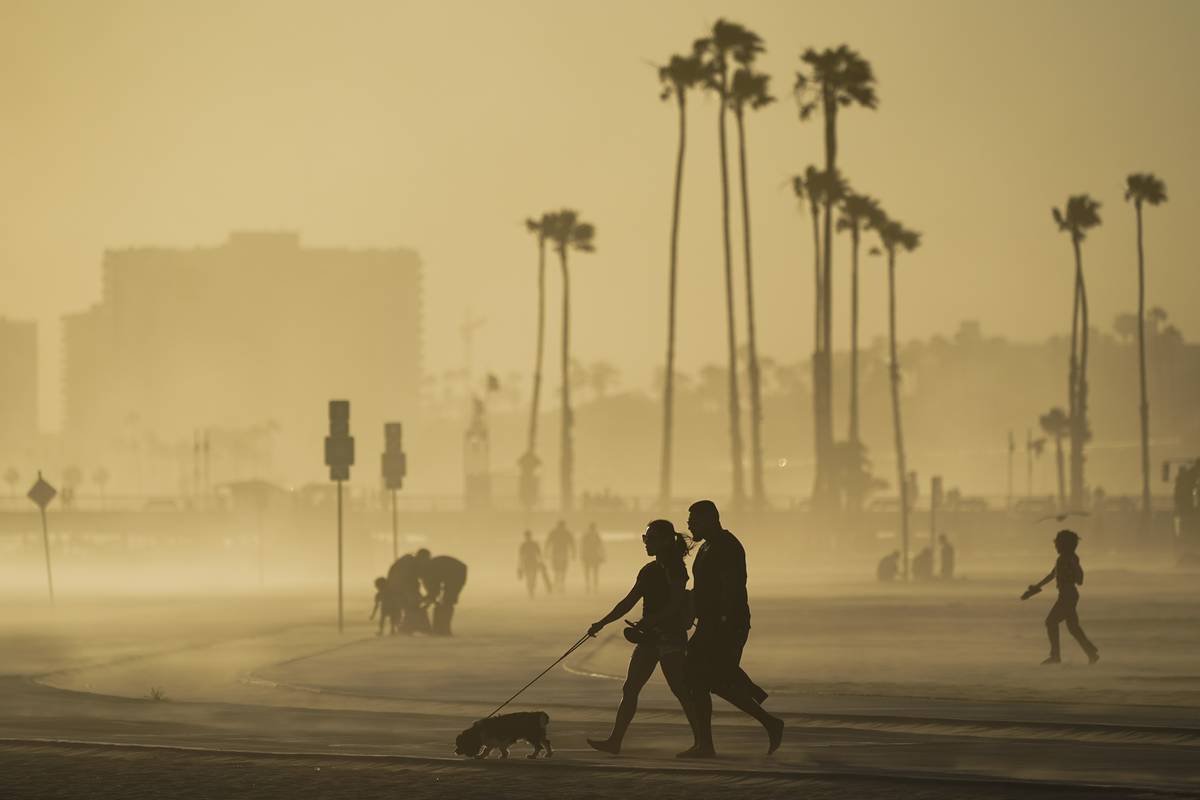 FILE - In this April 18, 2021, file photo, people walk on a beach path as evening winds kick up ...