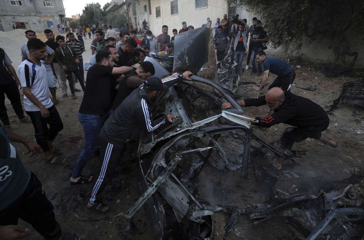 Palestinians gather around a car after it was hit by an Israeli airstrike, in Gaza City, Saturd ...