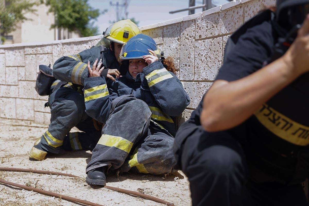 Israeli firefighters take cover as a siren sounds a warning of incoming rockets fired from the ...
