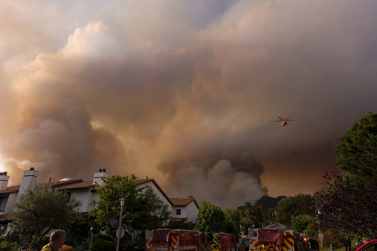 A firefighting helicopter drops water on a brush fire scorching at least 100 acres in the Pacif ...