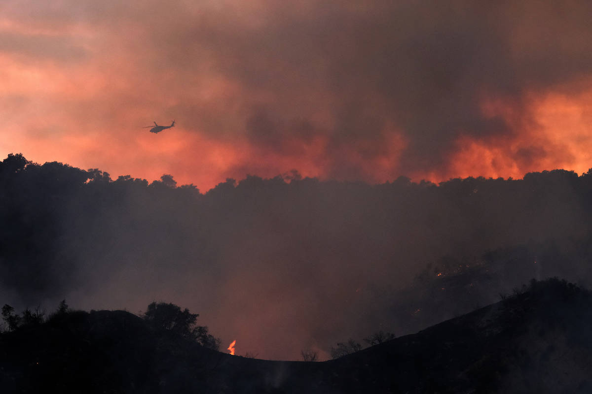 A firefighting helicopter prepares to drop water onto a brush fire scorching at least 100 acres ...