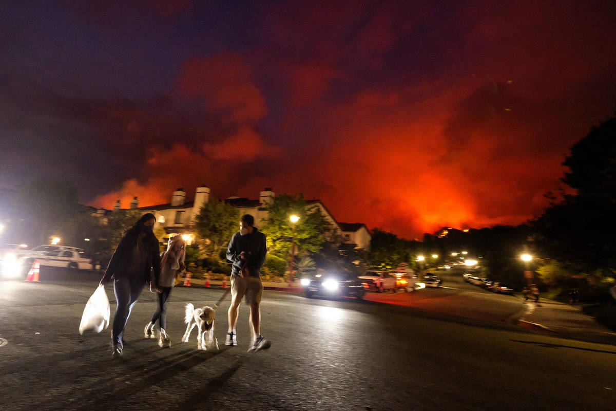 Residents walk a dog as a brush fire burns behind homes in the Pacific Palisades area of Los An ...